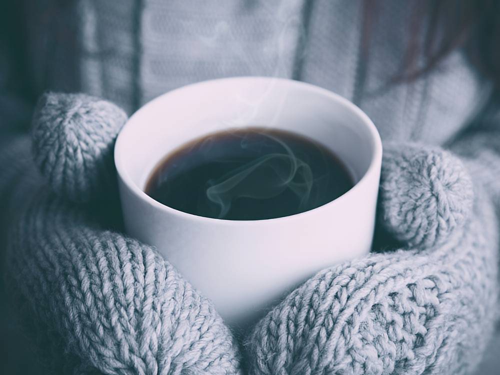 Hot cup of tea in being held in the hands of a person with knitted mittens